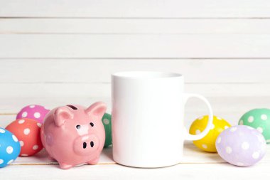 Paskalya yumurtalı beyaz kahve kupası ve beyaz ahşap arka planda domuz kumbarası. Metin veya tasarım için boşluk.