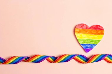 LGBT gökkuşağı kurdelesi ve pembe arka planda kağıt gökkuşağı kalbi. Gurur bant sembolü. Cinsiyet eşitliği kavramı. Metin için alanı kopyala.