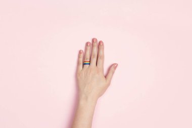 Pembe arka planda gökkuşağı kurdelesinden alyansı olan bir kadın eli. Lezbiyen evlilik teklifi. LGBT ailesi, gurur ayı. 