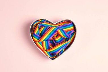 Pembe arka planda kalp şeklinde LGBT gökkuşağı kurdelesi. Gurur bant sembolü.