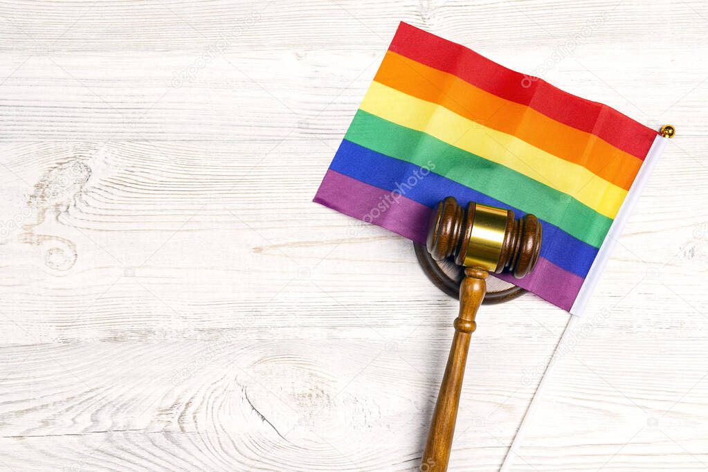 Woden judge gavel symbol of law and justice with lgbt flag in rainbow colours on wooden background. LGBT rights, justice and law equality concept