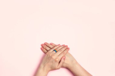 Pembe arka planda gökkuşağı kurdelesinden alyans takan kadın elleri. Lezbiyen evlilik teklifi. LGBT ailesi, gurur ayı. 