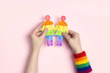 Igbt bilekliği olan kadın elleri pembe arka planda gökkuşağı bayrağı olan lezbiyen çift figürlerini tutuyor. LGBT gururu.