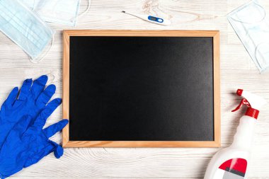 Eldivenler, tıbbi maske, antiseptik ve ahşap arka planda termometre ile çevrili temiz bir karatahta. Kopyalama alanı olan üst görünüm. Coronavirus koruması.