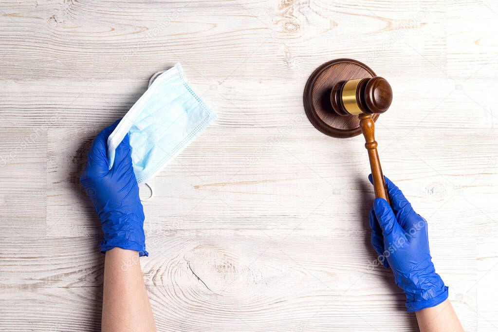 Hands of a judge in a medical glove holds face mask and gavel to protect from coronavirus. Judicial system and law during the coronavirus.