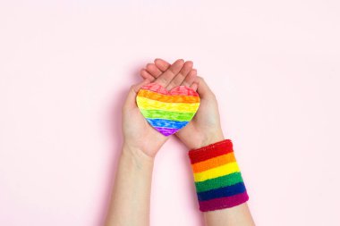 Kadın elleri pembe arka planda gökkuşağı LGBT kalbini tutuyor. Homoseksüel ve lgbt kavramı.