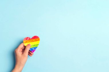 Mavi arka planda, gökkuşağı renkli LGBT kalp tutan kadın eli. Uzayı metin için kopyala. Homoseksüel ve lgbt kavramı.