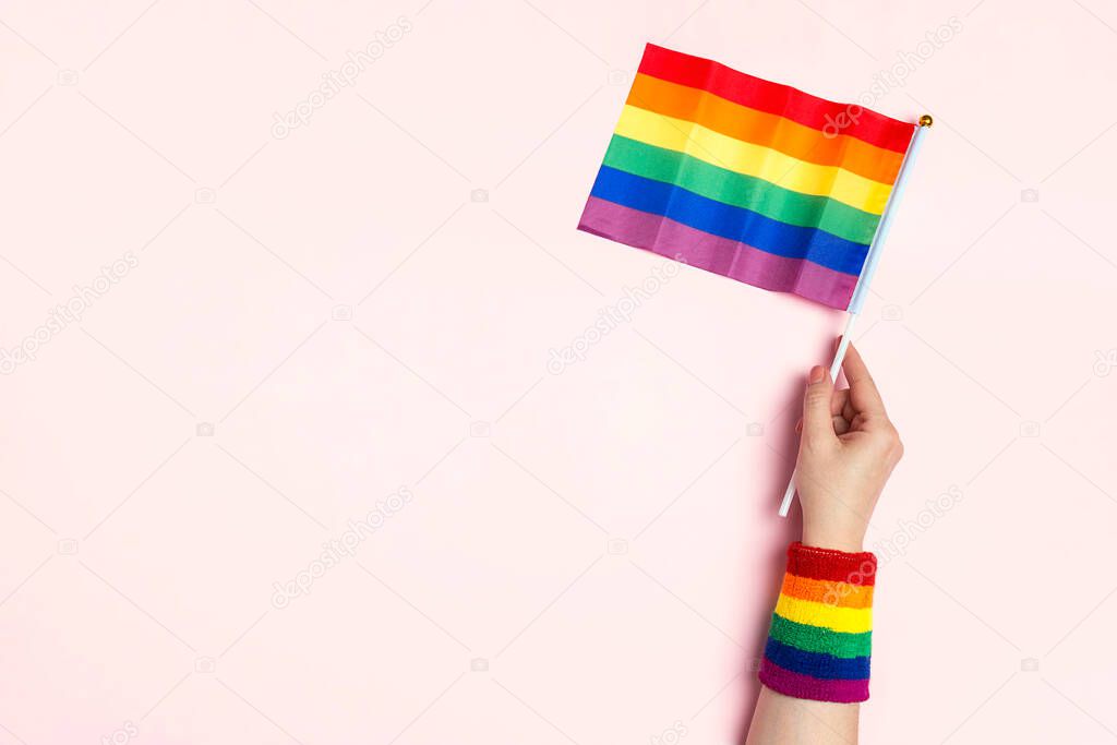 Female hand hold rainbow LGBT flag on a pink background. Homosexual and lgbt concept. Copy pace for text.