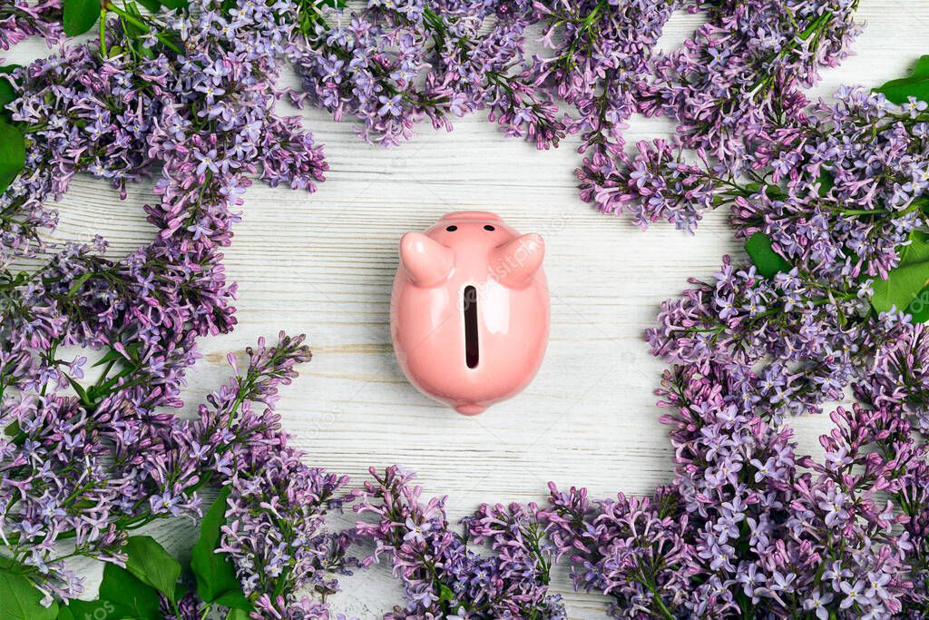 Piggy bank with lilac flowers on light wooden table. Saving money for spring holidays.