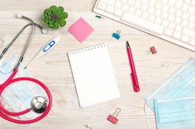 Boş not defteri, steteskop, klavye, termometre, maske, bitki ve malzeme ile beyaz ahşap masa. Üst görünüm, düz görünüm, çerçeve, kopyalama alanı.