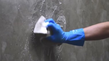 Mavi lastik eldiven giyen yakın plan bir sünger kullanarak beton duvarı temizliyor..
