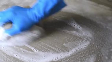 Mavi lastik eldiven giyen bir adam fayansları temizlemek için sünger kullanıyor..