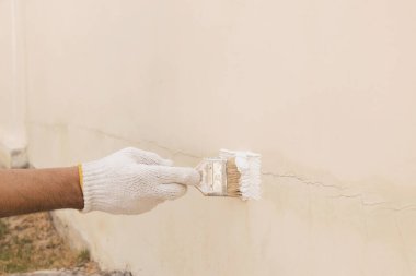 Boyayı beton duvardaki çatlakları kapatmak için kullanılan beyaz bez eldivenli bir eli kapat..