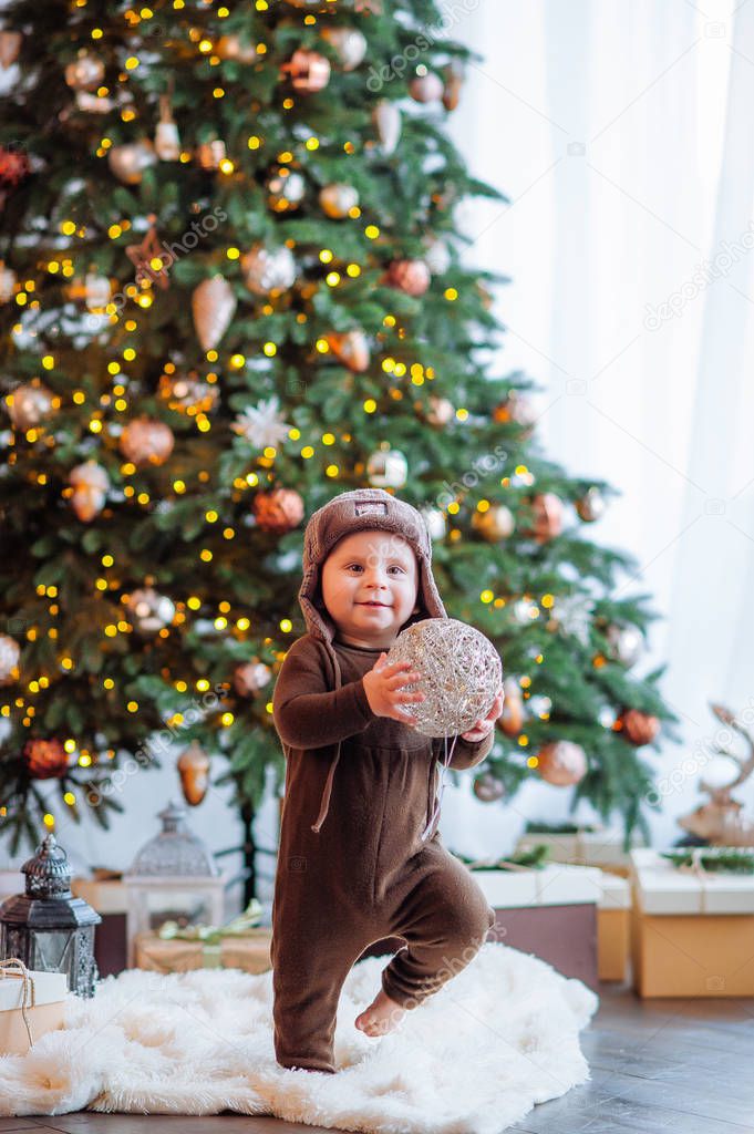 New year's photo session of a small one-year-old baby in a hat, Christmas tree, gifts