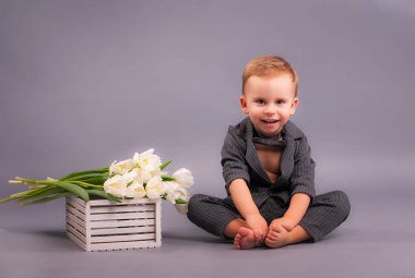Stüdyoda bir buket lale taşıyan küçük bir beyefendi, 8 Mart bayramının onuruna gri bir arka planda tüm anneler, büyükanneler, kızlar ve kızlar şeklinde bir tebrik kartı taşıyor.