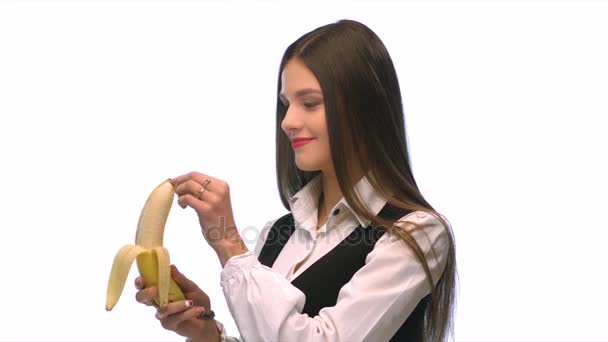 Chica morena en un traje de negocios sobre un fondo blanco comiendo un plátano con sonido — Vídeos de Stock