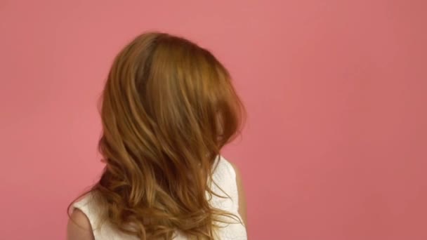 Красива дівчина-підліток з червоним дме волоссям і блакитними очима на рожевому фоні — стокове відео