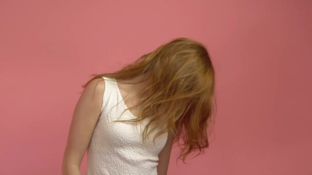 Menina adolescente bonita com cabelo vermelho soprando e olhos azuis no fundo rosa — Vídeo de Stock