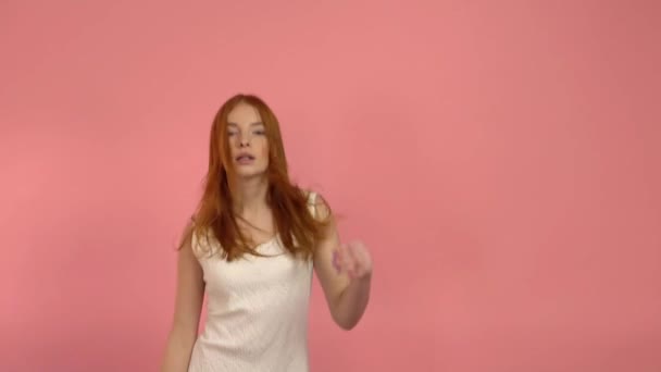 Девушка-подросток с рыжими волосами прыгает на розовом фоне — стоковое видео