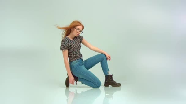 Hermosa chica pelirroja con gafas sobre un fondo blanco — Vídeos de Stock