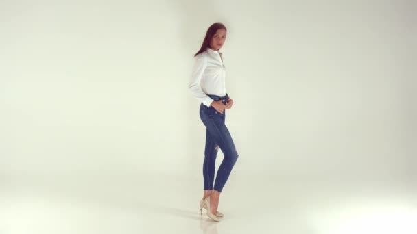 Una chica joven y feliz en jeans con estilo sobre un fondo blanco — Vídeo de stock