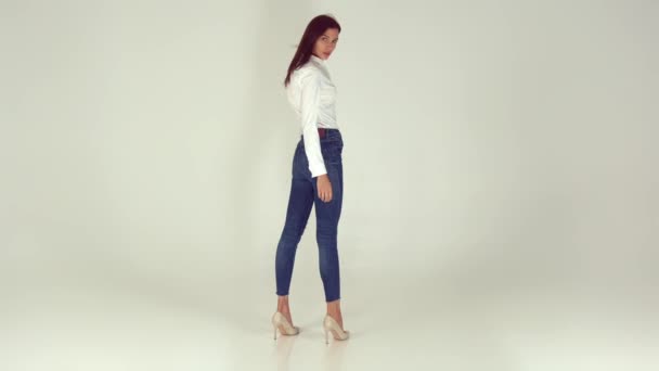Una chica joven y feliz en jeans con estilo sobre un fondo blanco — Vídeos de Stock