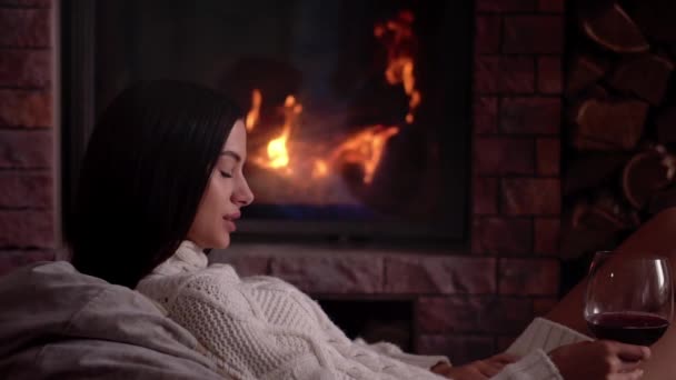 Young woman sitting at home by the fireplace and drinking a red wine. — Stock Video