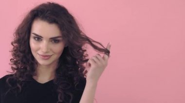 Siyah T-shirt uzun kıvırcık saçlı güzel moda kız. Kız pembe bir arka plan üzerinde stüdyoda. Reklam, saç ürünleri, güzellik salonları, kozmetik, giyim. Moda, butik. Pembe.