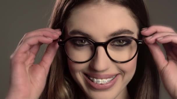 Retrato interior de una joven guapa en gafas redondas con tirantes sobre fondo gris — Vídeos de Stock