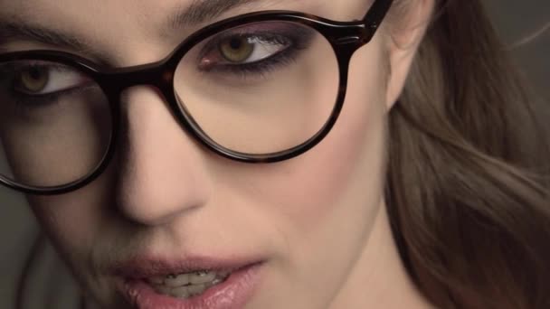 Крытый портрет молодой красивой девушки в круглых очках с брекетами на сером фоне — стоковое видео