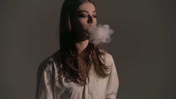 Mädchen mit einem Vaporizer auf einem grauen Hintergrund, der E-Zigarette dampft — Stockvideo