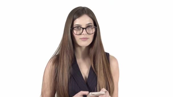 Молодая женщина в очках, изолированных на белом фоне, улыбается, с телефоном — стоковое видео