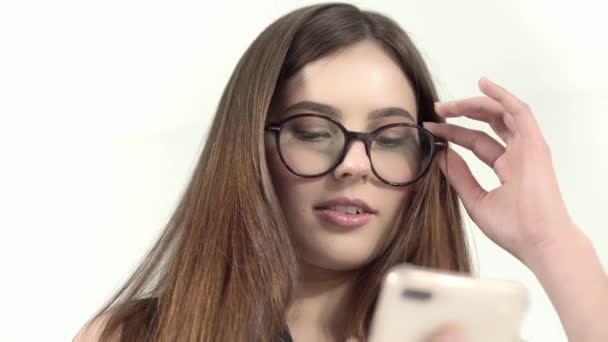 , Telefon ile gülümseyen genç kadın üzerinde beyaz bir arka plan üzerinde izole trasparent gözlük — Stok video