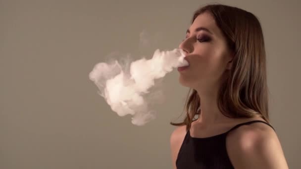 Mädchen mit einem Vaporizer auf einem grauen Hintergrund, der E-Zigarette dampft — Stockvideo