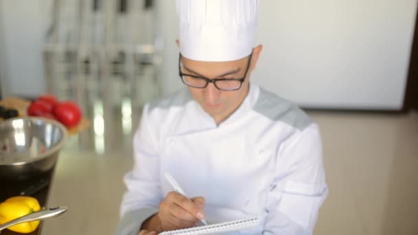 Mannelijke chef-kok in een commerciële keuken zittend op de moed en het schrijven van een reciepe — Stockvideo