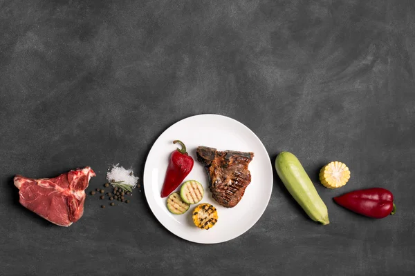 Gegrilltes Steak auf schwarzer Tafel mit Gemüse und Gewürzen — Stockfoto