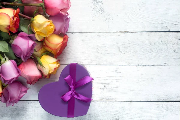 Фиолетовые и желтые розы, коробка присутствует на белом деревянном фоне — стоковое фото