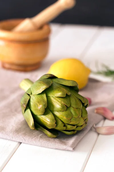Artischocken und Zitrone auf Holztisch mit Serviette und Mörser. Artischocken haben eine der höchsten antioxidativen Kapazitäten für Gemüse. — Stockfoto
