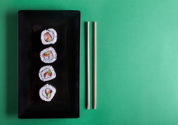 Японские суши на зеленом фоне. Роллы и палочки для еды — стоковое фото