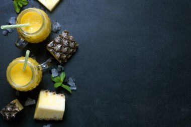 Taze ananas smoothie meyve rustik siyah bir arka plan ile gözlük. Yat ve erimiş buz boşlukla kopyalayın