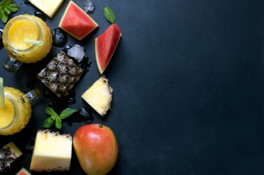 Taze ananas ve mango smoothie meyve rustik siyah bir arka plan ile gözlük