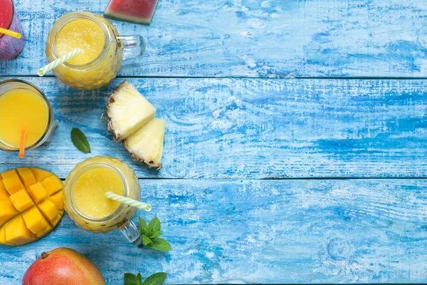Свіжий ананас і манго в трьох келихах з соломинками з фруктами на синьому дерев'яному сільському фоні. копіювання простору — стокове фото