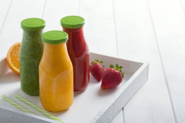 Taze çilek, portakal ve brokoli smoothie meyve ve sebze Beyaz ahşap rustik zemin üzerinde şişelerde