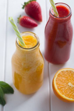 Beyaz ahşap rustik zemin üzerinde meyve ile şişelerde taze çilek, portakal güler yüzlü