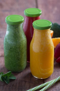 Taze çilek, portakal ve brokoli smoothie meyve ve sebze kahverengi ahşap rustik arka plan üzerinde şişelerde. Dikey yakın çekim