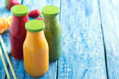 Taze çilek, portakal ve brokoli güler yüzlü bir mavi ahşap rustik arka plan üzerinde sebze ve meyve ile şişelerde kadar yakın ve alanı Kopyala