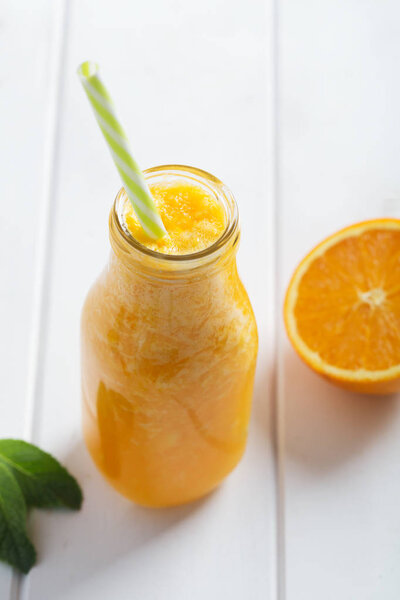 Fresh orange smoothie in bottle on a white wooden rustic background