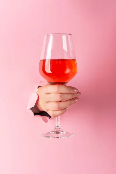 एक महिला अपने हाथ में नारंगी शराब का एक ग्लास रखती है, टूटे हुए कागज में एक छेद के माध्यम से डाला जाता है — स्टॉक फ़ोटो, इमेज