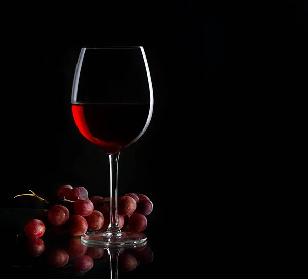 Egy pohár vörösbor és egy csomó szőlő a sötét háttérben. — Stock Fotó