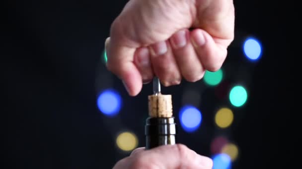 Hombre abriendo una botella de vino tinto en el fondo festivo oscuro con bokeh colorido — Vídeos de Stock